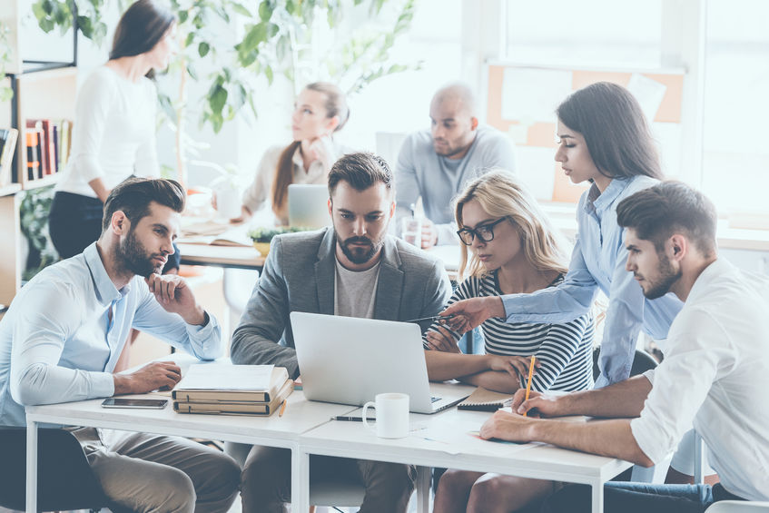 59746317 - group of young business people working and communicating while sitting at the office desk together with colleagues sitting in the background