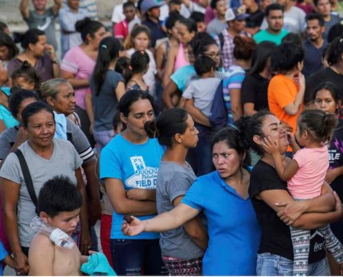 Migrants, many of whom were returned to Mexico under the Trump administration's "Remain in Mexico" policy, wait in line to get a meal in an encampment near the Gateway International Bridge in Matamoros, on the Mexico-U.S. border, August 30, 2019. (Photo courtesy Voice of America) Public domain  