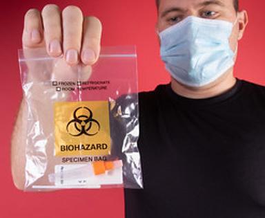Man wearing a face mask holds a palstic Biohazard specimen bag containing a used covid test. Both the mask and the specimen bag are headed for waste disposal. September 29, 2021 (Photo by Jernej Furman) Creative Commons via Flickr